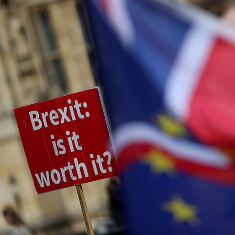 Eine EU- und eine Großbritannienflagge. Im Hintergrund ein Protestschild mit der Aufschrift "Brexit: is it worth it?"