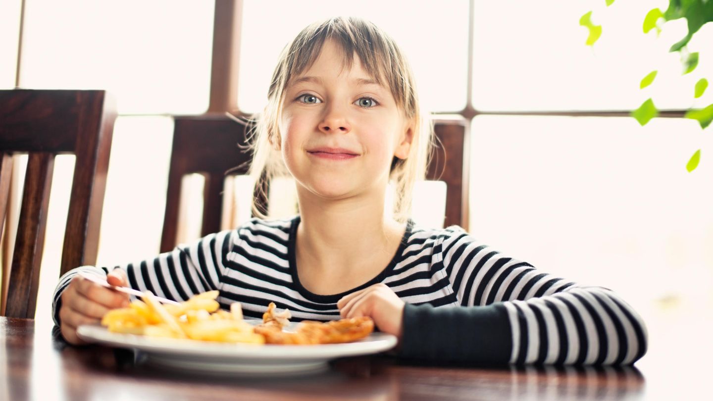 Ein Mädchen isst Pommes frites und strahlt in die Kamera
