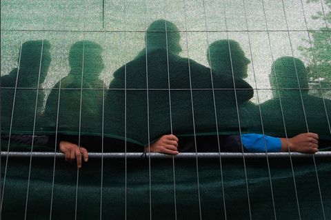 Mehrere Männer stehen hinter einem verdeckten Zaun in einer Flüchtlingsunterkunft
