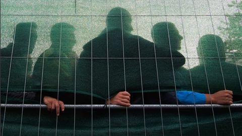 Mehrere Männer stehen hinter einem verdeckten Zaun in einer Flüchtlingsunterkunft