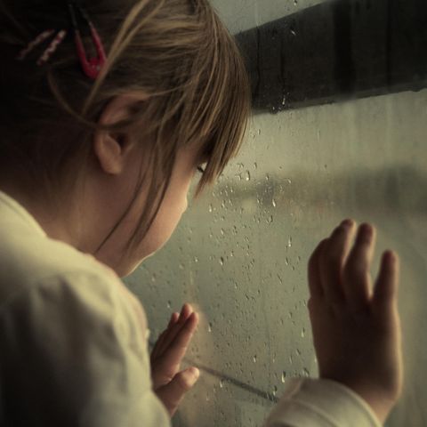 Kind steht am Fenster und guckt raus, es regnet