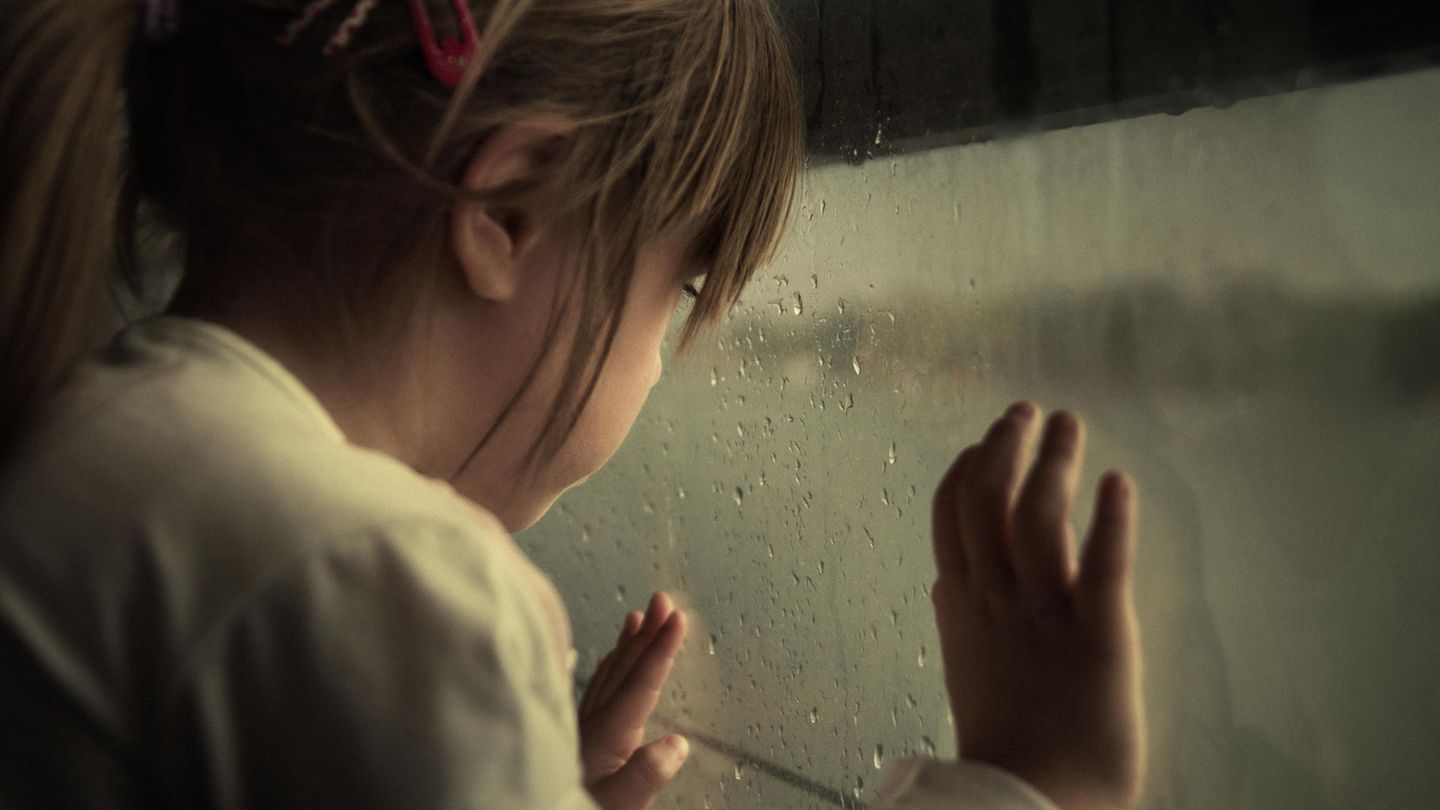 Kind steht am Fenster und guckt raus, es regnet
