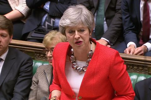Premierministerin Theresa May steht im roten Blaser im Unterhaus und hebt beschwichtigend beide Hände