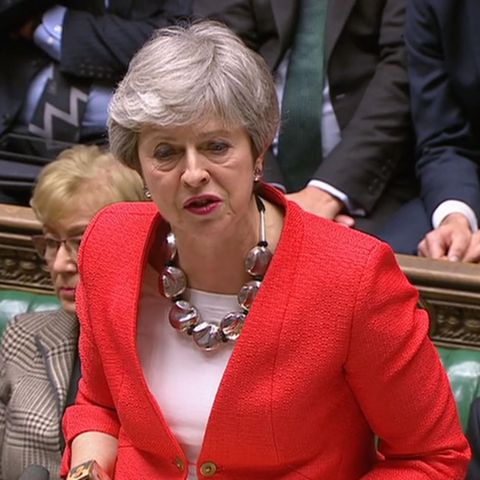 Premierministerin Theresa May steht im roten Blaser im Unterhaus und hebt beschwichtigend beide Hände