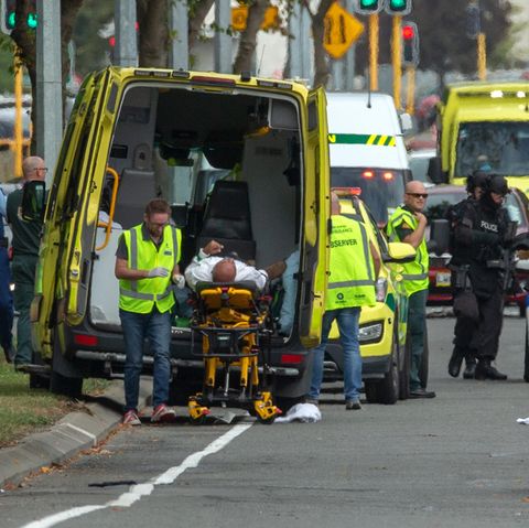 Ein Verletzter wird in Christchurch in einen Krankenwagen geladen, während schwer bewaffnete Polizisten vorbeigehen