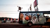 Sky springt mit dem Skateboard vom Autodach eines Tourbusses