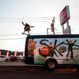 Sky springt mit dem Skateboard vom Autodach eines Tourbusses