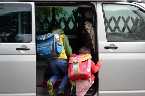 Zwei Grundschulkinder mit Ranzen auf dem Rücken steigen in die Schiebetür eines silbernen VW-Busses