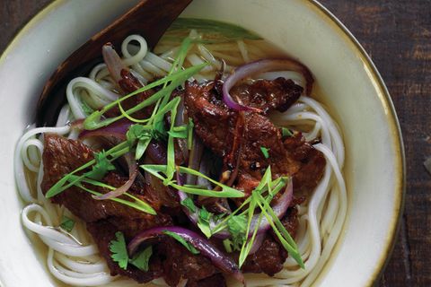 Wok-geküsste Rindfleisch-Pho      Zutaten:  300 g getrocknete, mittelflache Reisbandnudeln oder 450 g frische Pho-Nudeln, 2 EL plus 1 TL Rapsöl oder ein anderes neutrales Öl, bei Bedarf mehr, 350 g sauber pariertes Schwanzstück vom Rind oder ein Flanksteak, quer über die Maserung in mundgerechte, nur 6 mm dicke Stücke geschnitten, ¼ TL frisch gemahlener schwarzer Pfeffer, bei Bedarf mehr, ¾ TL Zucker, 1 TL Maisstärke, 2 TL Fischsauce, bei Bedarf mehr, 2 TL normale Sojasauce, 2 l Rindfleisch-Pho-Brühe, Salz, 2 Knoblauchzehen, fein gehackt, ½ kleine (60 g) gelbe oder rote Zwiebel, entlang der Maserung in schmale Stücke geschnitten, 2 schlanke grüne Zwiebeln (weiße und grüne Teile), scharf diagonal in lange, dünne Stücke geschnitten, 5 g gehacktes frisches Koriandergrün      Zubereitung:  Getrocknete Nudeln in einem Topf mit Wasser 5 bis 7 Minuten kochen, bis sie weich sind, aber noch Biss haben (oder richten Sie sich nach der Anleitung auf der Packung). Abtropfen lassen, restliche Stärke abspülen, dann erneut gut abtropfen lassen. Mit 1 TL des Öls vermengen, damit sie nicht klebrig werden, dann beiseitestellen. Frische Nudeln sind oft bereits eingefettet. Auseinanderziehen und beiseitestellen. Das Rindfleisch in einer Schüssel mit ¼ TL Pfeffer, Zucker, Maisstärke, Fischsauce und Sojasauce vermengen und beiseitestellen. Die Pho-Brühe in einem kleinen Topf wieder aufwärmen und mit Fischsauce und Salz nach Wunsch würzen. Wenn sie kocht, die Temperatur verringern und zudecken. Nudeln und Rindfleisch mit Knoblauch, Zwiebel, grüner Zwiebel und Koriandergrün neben den Herd stellen. Den Teller mit den Garnierungen und/oder den Knoblauchessig auf den Tisch stellen. Zum Kochen einen großen, gut gewürzten Wok oder eine Bratpfanne mit Antihaftbeschichtung verwenden. Bei mittlerer oder etwas stärkerer Temperatur erhitzen. Einen kleinen Spritzer Öl dazugeben, wenn Sie fürchten, dass die Nudeln verkleben. Nudeln dazugeben und etwa 1 Minute anbraten, bis sie etwas weich werden und zu verkleben beginnen. Dann vom Herd nehmen und auf vier Suppenschalen verteilen. Wenn nötig, den Wok (oder die Pfanne) spülen und trocknen, dann bei mittlerer oder etwas höherer Temperatur erhitzen. Die restlichen 2 EL Öl einrühren. Knoblauch und Zwiebel dazugeben. Sobald sie duften, nach etwa 30 Sekunden, die Aromastoffe an einer Seite der Pfanne aufhäufen. Die Temperatur auf hoch einstellen, das Rindfleisch hineingeben und einschichtig verteilen. Etwa 1 Minute ungestört kochen lassen. Wenn das Fleisch braun zu werden beginnt, mit einem Bratenheber wenden; dann 1 bis 2 Minuten umrühren. Das Fleisch sollte noch ein wenig roh sein. Das Rindfleisch auf die Schalen verteilen und mit der grünen Zwiebel und dem Koriandergrün garnieren. Leicht mit Pfeffer bestreuen. Die Brühe kosten, bei Bedarf abschmecken, dann aufkochen und in die Schalen schöpfen. Sofort mit den Extras servieren und wie andere Pho-Suppen genießen.