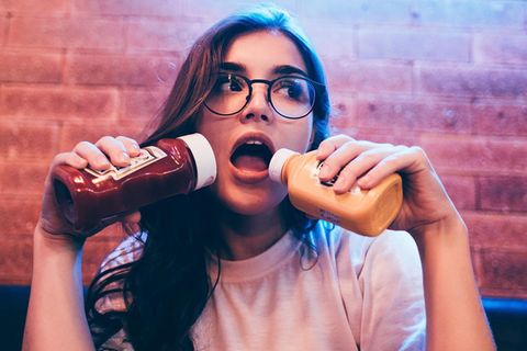 Gesunde Ernährung: Junge Frau hält sich zwei Flaschen Ketchup vor den Mund