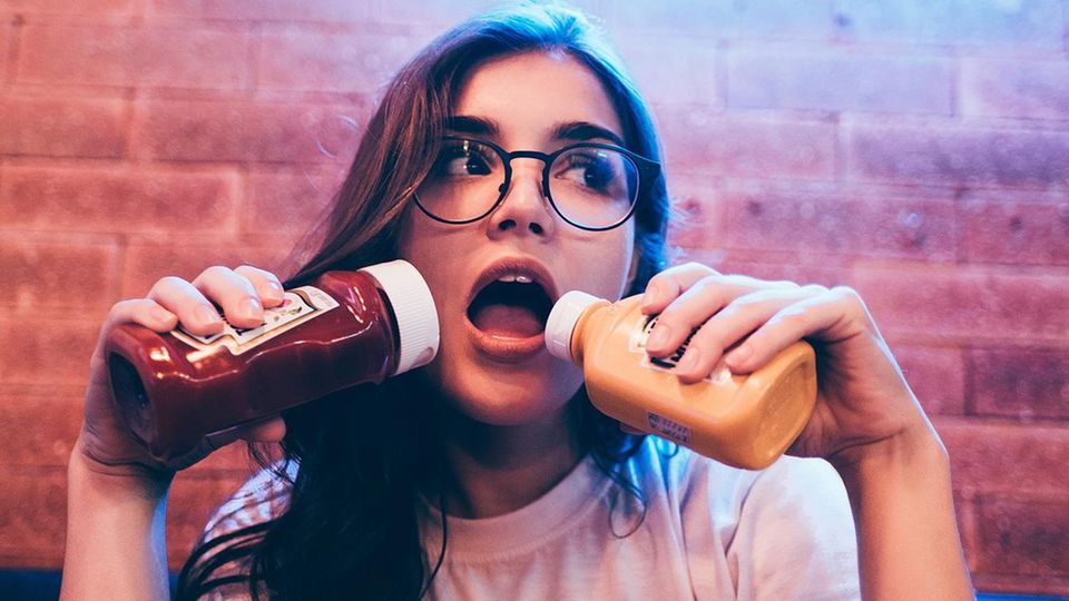 Gesunde Ernährung: Junge Frau hält sich zwei Flaschen Ketchup vor den Mund
