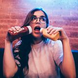 Gesunde Ernährung: Junge Frau hält sich zwei Flaschen Ketchup vor den Mund