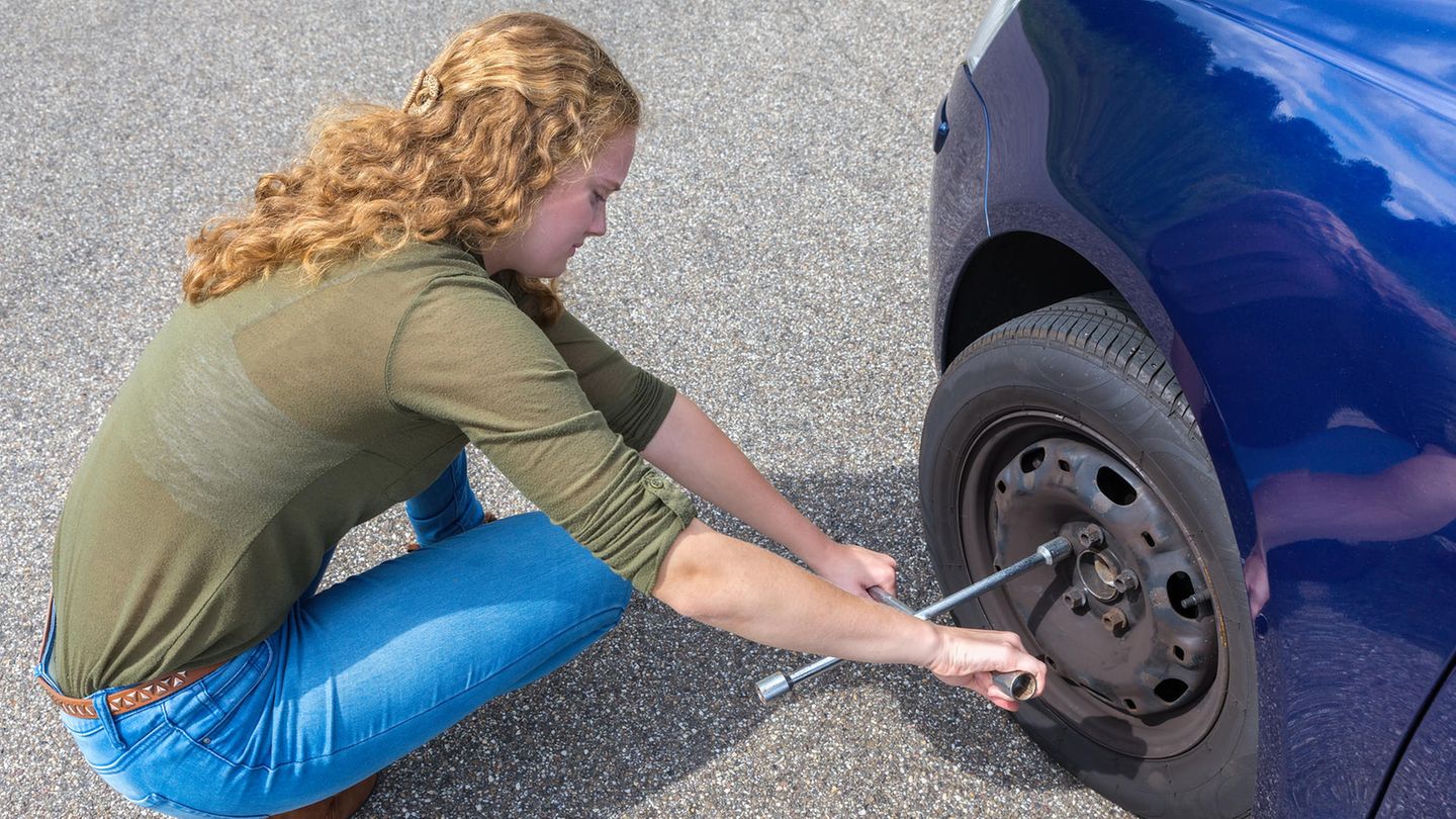 Eine junge Frau löst die Schrauben an einem Autoreifen, um den Reifen zu wechseln