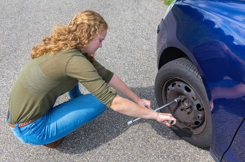 Eine junge Frau löst die Schrauben an einem Autoreifen, um den Reifen zu wechseln