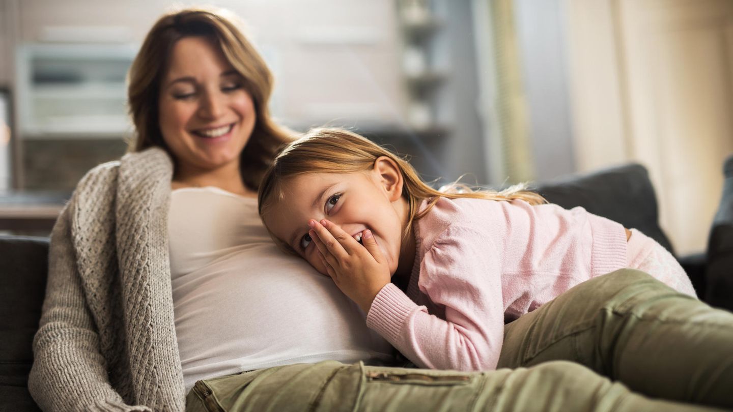 Ein Mädchen legt seinen Kopf auf den Bauch der schwangeren Mutter