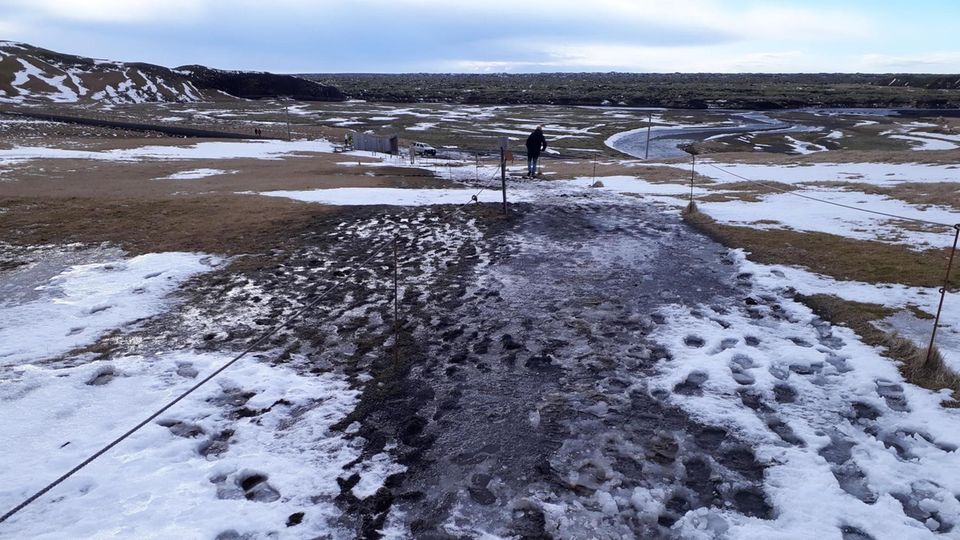 Fjaðrárgljúfur In Schnee und Matsch sind hunderte Schuhabdrücke zu sehen, die zwischen zwei aufgespannten Seilen Richtung Horizont führen
