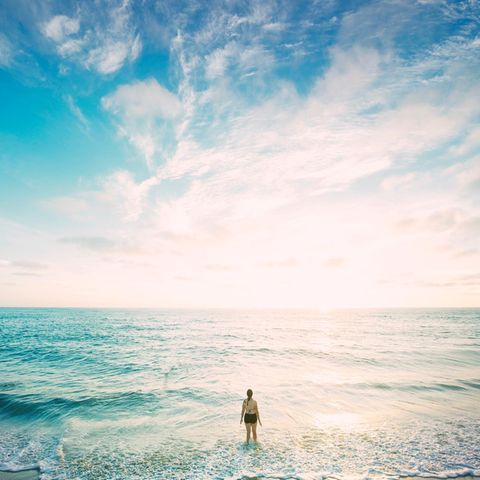 Frau steht am Strand mit Beinen im Wasser