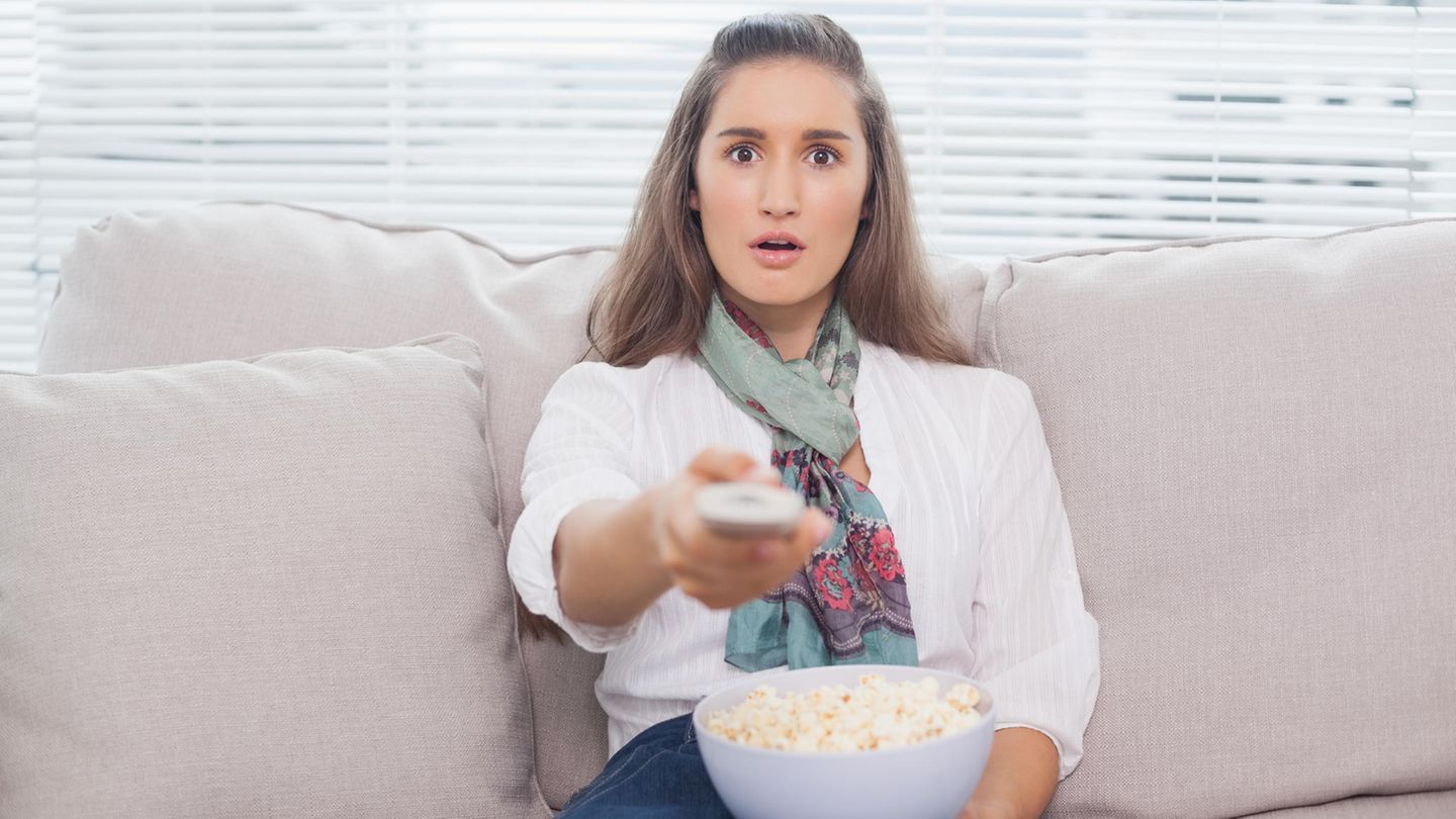 Junge Frau auf dem Sofa mit Popcorn und Fernbedienung