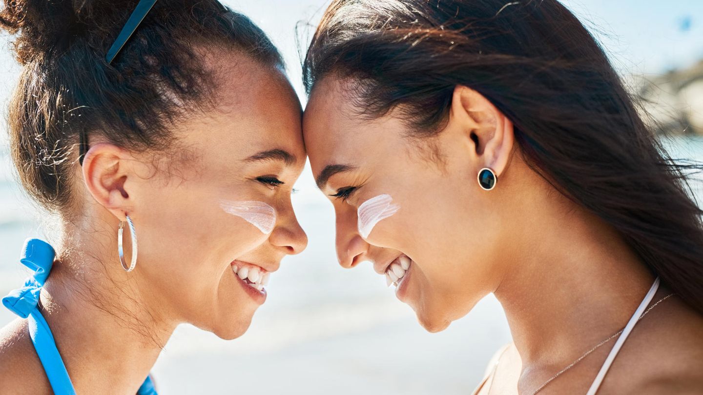 Zwei junge Frauen mit Sonnencreme auf den Wangen, stehen Stirn an Stirn und lächeln sich an