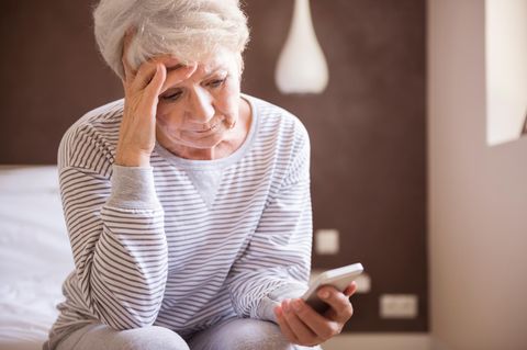 Eine alte Frau sitzt auf dem Bett uns starrt auf ihr Handy