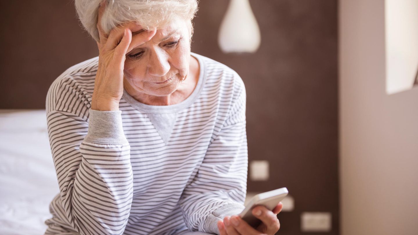Eine alte Frau sitzt auf dem Bett uns starrt auf ihr Handy