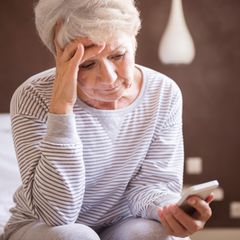 Eine alte Frau sitzt auf dem Bett uns starrt auf ihr Handy