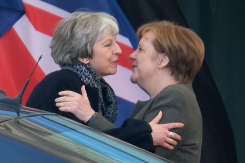 Theresa May und Angela Merkel umarmen sich zur Begrüßung vor dem Bundeskanzleramt. Davor ein Auto, dahinter der Union Jack