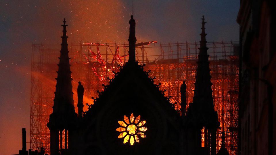 Hinter dem Giebel von Notre Dame mit seinem typischen Rosetten-Fenster erhellt Feuerschein den Himmel über Paris