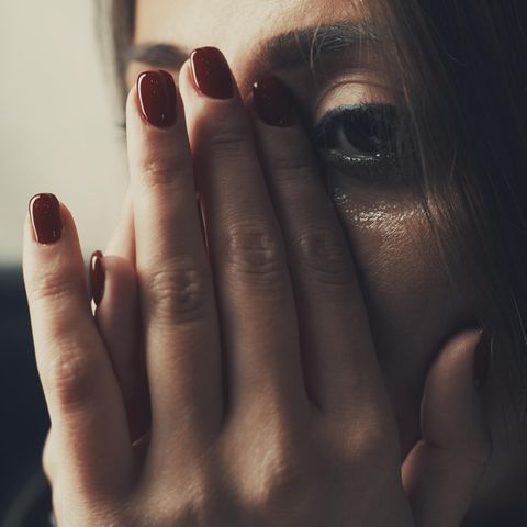 Nahaufnahme vom Gesicht einer Frau, die sich mit flacher Hand Tränen vom Gesicht wischt.