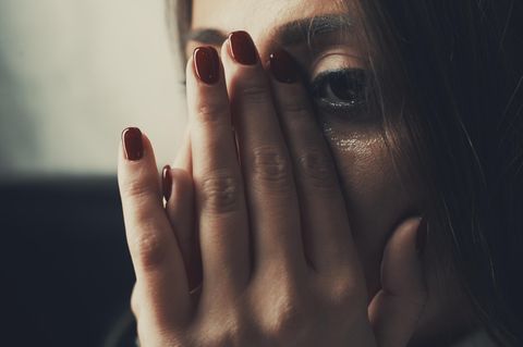 Nahaufnahme vom Gesicht einer Frau, die sich mit flacher Hand Tränen vom Gesicht wischt.
