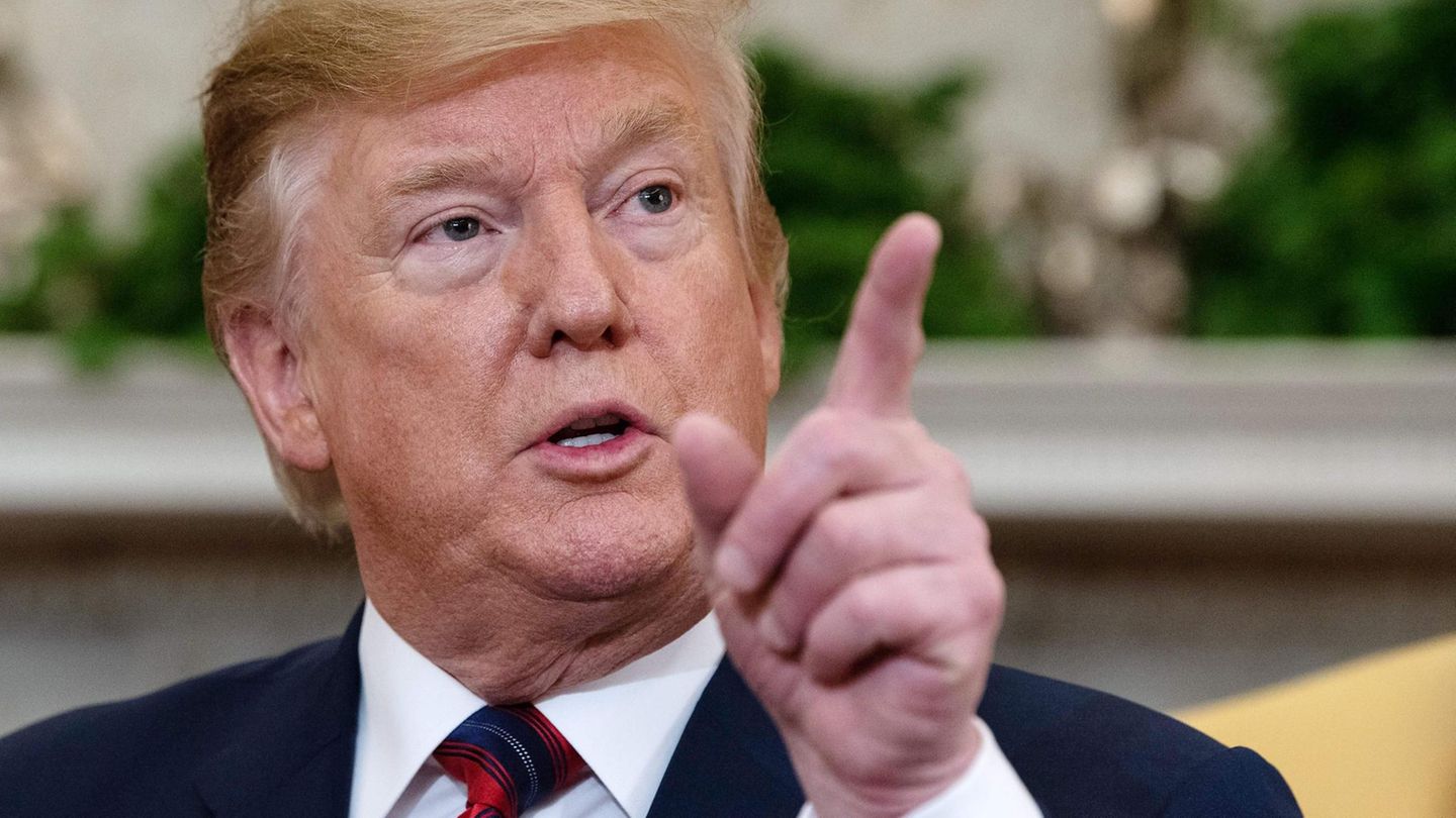 Donald Trump sitzt und zeigt mit seinem linken Zeigefinger in die Luft