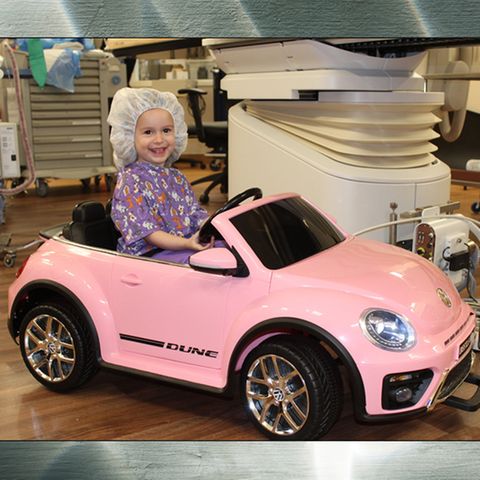 Kleinkind fährt einen pinken Spielzeug-VW-Beetle in den Operationssaal.