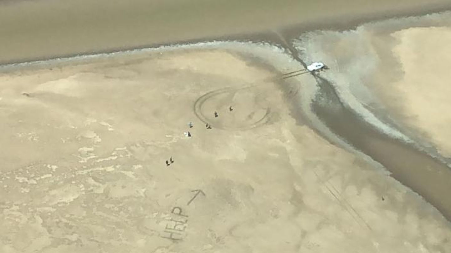 "Help" steht im Sand, ein Pfeil daneben weist auf einen weißen Pickup, der in einem Flussbett steht
