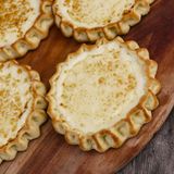 Casadinas al formaggio   Sardische Käsetörtchen   Für ca. 15 Stück · Zubereitung: 30–40 Minuten · Ruhezeit: einige Stunden · Backzeit: 30 Minuten Schwierigkeitsgrad: mittel      Zutaten:  Für den Teig: 400 g Hartweizengrieß, 100 g Schmalz, Salz      Für die Füllung: 500 g frischer Käse (oder Ricotta), gerieben, 100 g Zucker, 2 Eier (Größe M), Abrieb von 1 unbehandelten Zitrone (oder Orange), 100 g Rosinen, 50 g Weizenmehl (Type 405)      Außerdem: etwas Honig zum Bestreichen      Zubereitung:  Hartweizengrieß, Schmalz, etwas Salz und etwas lauwarmes Wasser zu einem geschmeidigen Teig verarbeiten. Diesen mit einem Küchentuch abdecken und einige Stunden ruhen lassen. Den Backofen auf 150 °C Ober-/Unterhitze vorheizen. In einer Schüssel den geriebenen Käse gut mit Zucker, Eiern, Zitronenabrieb und Rosinen vermischen. Etwas Mehl untermischen, damit die Füllung die richtige Konsistenz erhält. Den Teig dünn ausrollen und Kreise mit einem Durchmesser von etwa 10 cm ausstechen. Darauf jeweils einen Löffel der Füllung geben. Die Teigränder etwas hochklappen und an mehreren Stellen zusammenkneifen, um eine Schalenform zu bilden. Die Casadinas auf einem mit Backpapier ausgelegten Backblech platzieren und im vorgeheizten Ofen in etwa 30 Minuten goldbraun backen. Aus dem Ofen nehmen und mit etwas Honig bestreichen. Casadinas werden normalerweise lauwarm serviert.