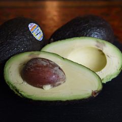 Eine aufgeschnittene Avocado liegt vor zwei weiteren Avocados
