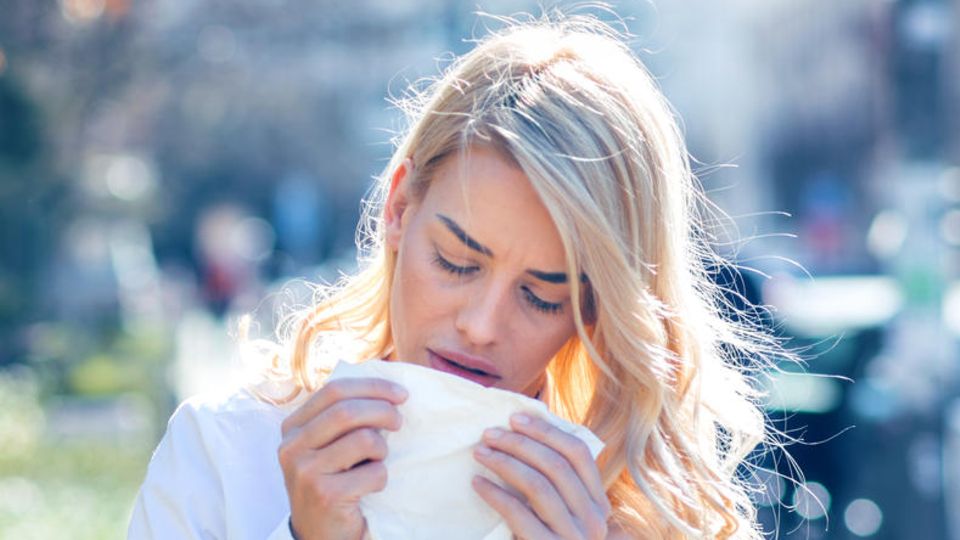 Pollenallergie und Heuschnupfen: Eine Frau niest in ein Taschentuch