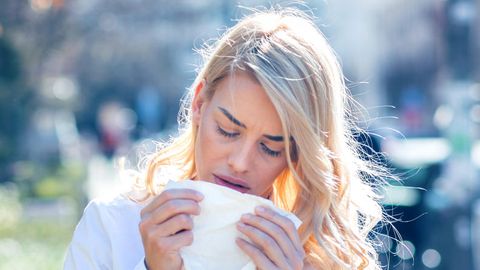 Heuschnupfen: Eine Frau niest in ein Taschentuch