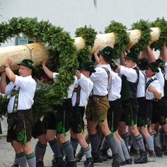 Männer in Trachten stellen einen Maibaum auf