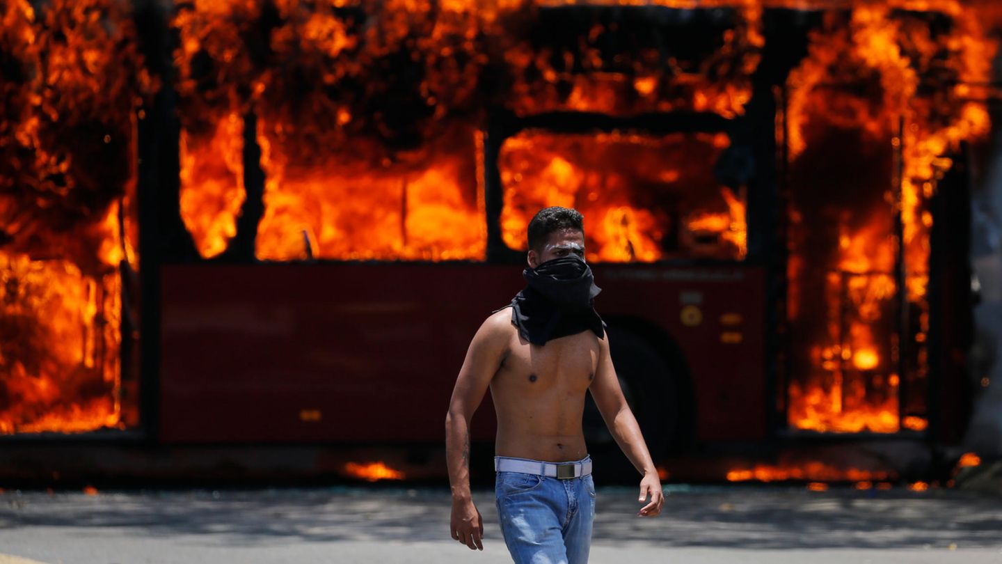 Venezuela, Caracas: Ein Demonstrant geht vor einem Bus