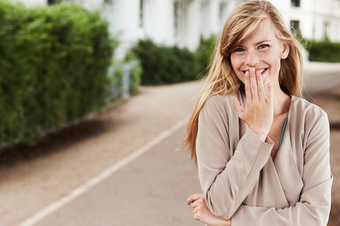 Eine junge Frau lacht und hält sich dabei die Hand vor den Mund