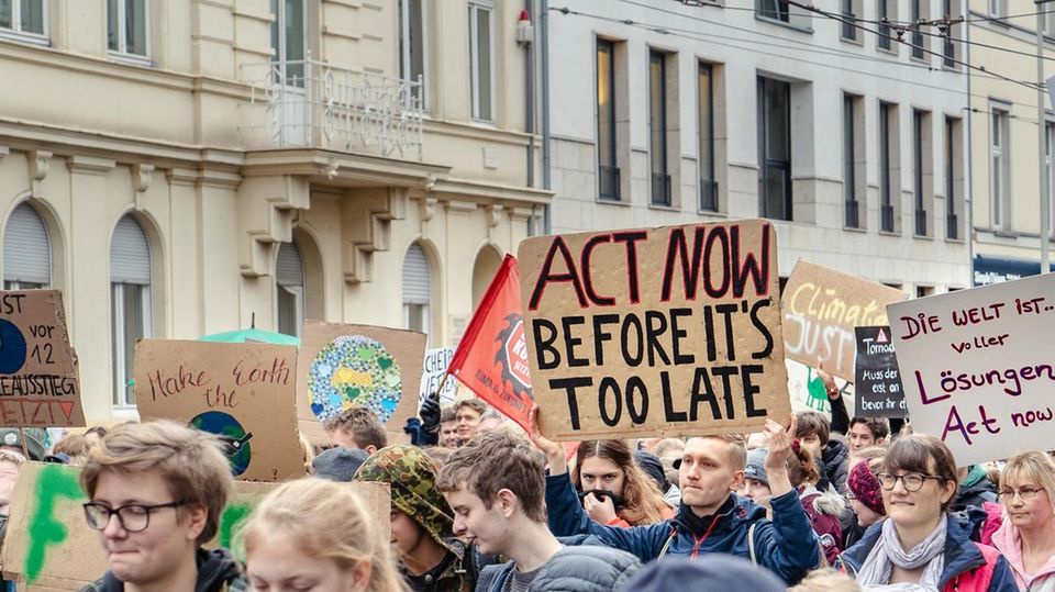 Auf Demo gegen den Klimawandel hält ein Mann ein Schild mit der Aufschrift "Act now before it's too late".
