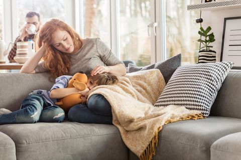 Mutter sitzt mit krankem Kind auf Sofa
