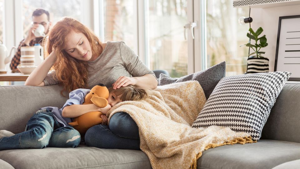 Mutter sitzt mit krankem Kind auf Sofa
