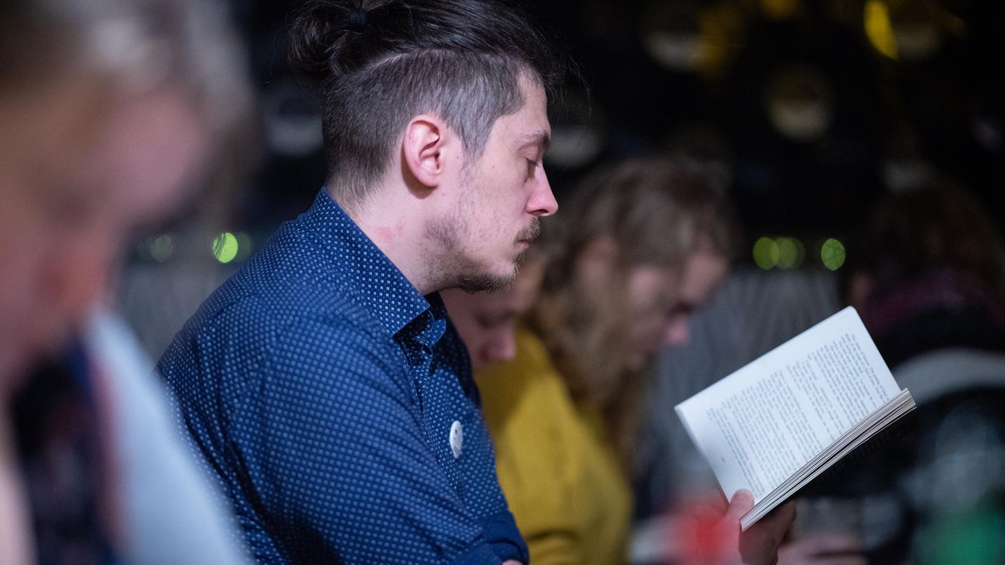 Ein Mann im blauen Hemd hät ein aufgeschlagenes Buch vor sich und liest