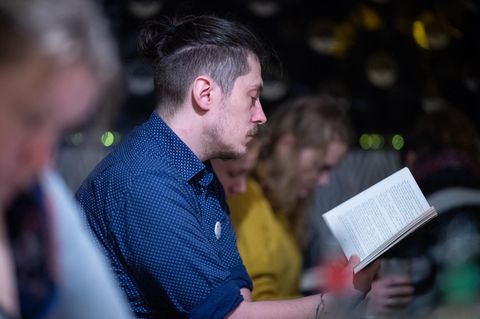 Ein Mann im blauen Hemd hät ein aufgeschlagenes Buch vor sich und liest