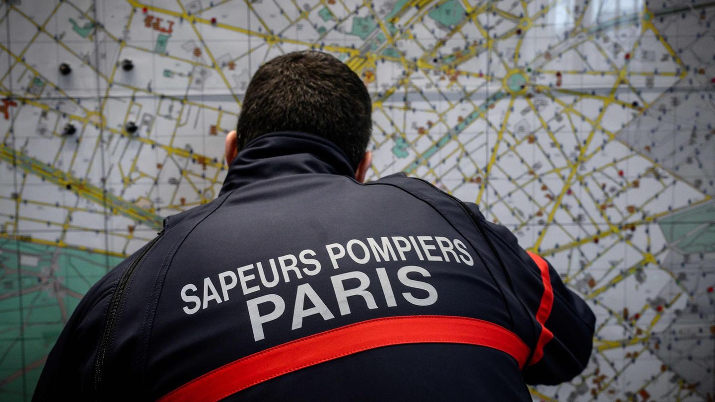 Ein Feuerwehrmann in dunkelblauer Jacke mit "Sapeurs Pompiers Paris" auf dem Rücken betrachtet einen Stadtplan von Paris