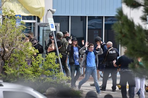 Zwischen Polizisten in schwerer Schutzkleidung laufen Schüler mit erhobenen Händen aus einem Gebäude
