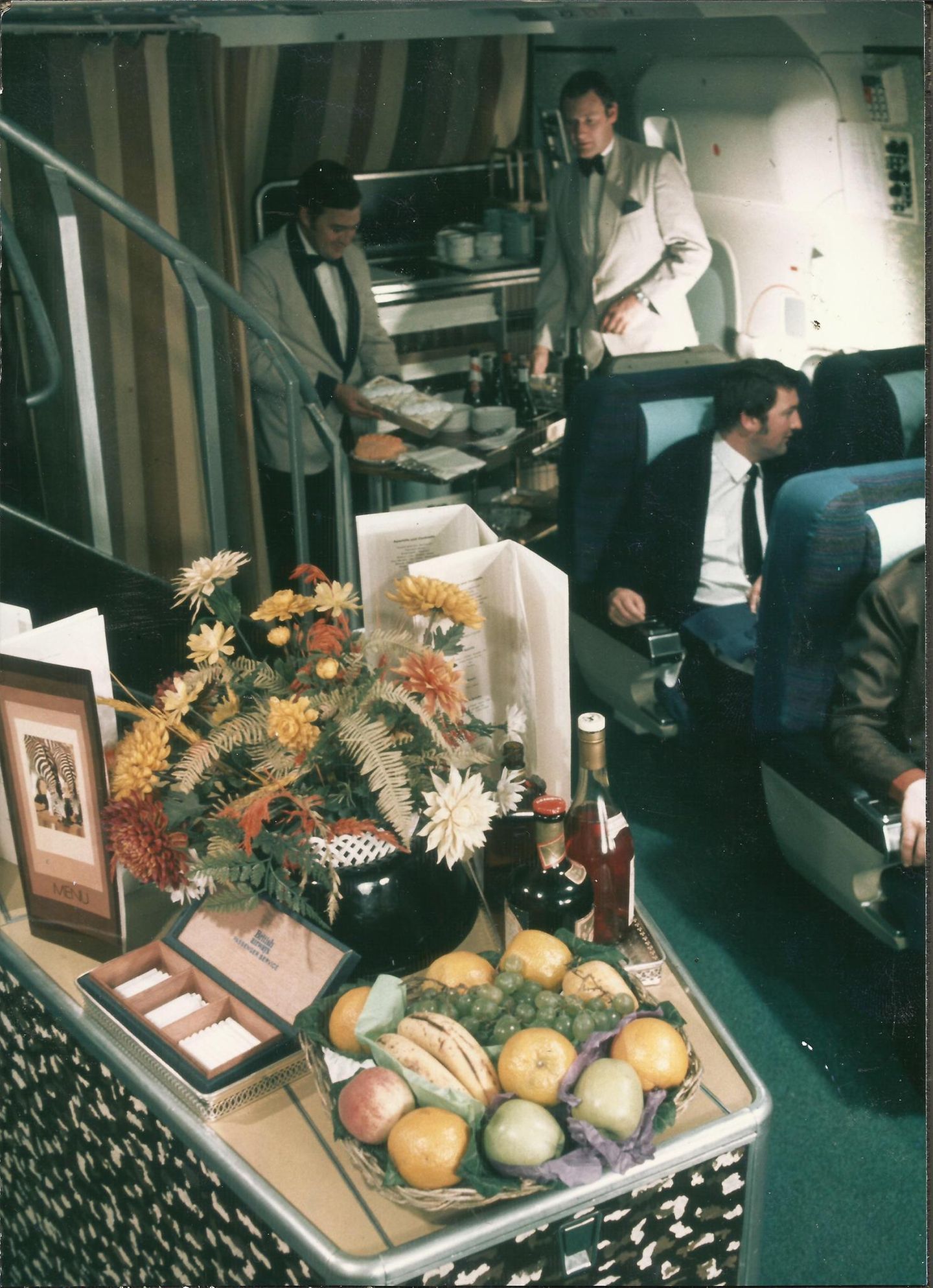 Ein Blick zurück vom Bug der Boeing 747 zur Treppe in der First Class, die zum Upper Deck führt. Auf dem Podest sind Früchte, Alkoholika und Zigaretten drapiert. Rauchen an Bord war Mitte der 1970er Jahre noch erlaubt, als dieses Foto entstand.