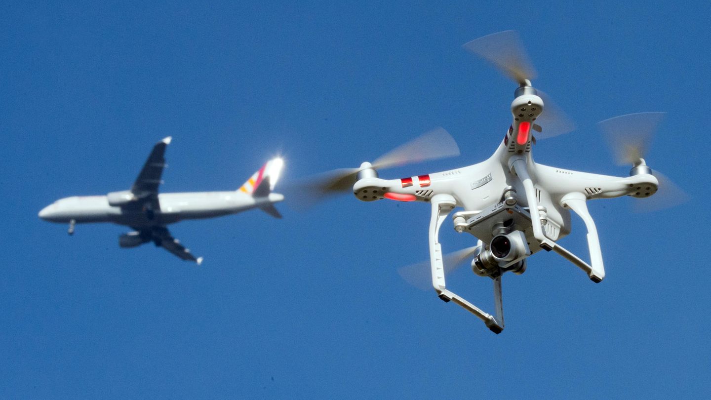 In der Umgebung eines deutschen Flughafens: Eine private Drohne fliegt in knapp zehn Metern Flughöhe über einem Garten, als in weiter Entfernung ein Flugzeug zu sehen ist.