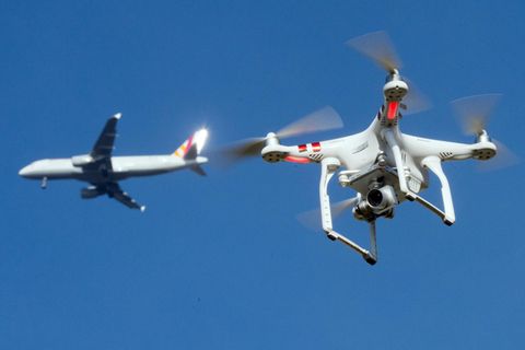 In der Umgebung eines deutschen Flughafens: Eine private Drohne fliegt in knapp zehn Metern Flughöhe über einem Garten, als in weiter Entfernung ein Flugzeug zu sehen ist.